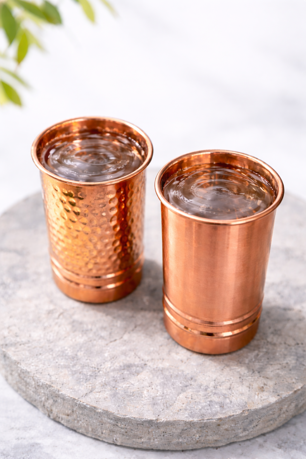 Tāmpatra copper glasses, hammered and plain, filled with water on a stone coaster