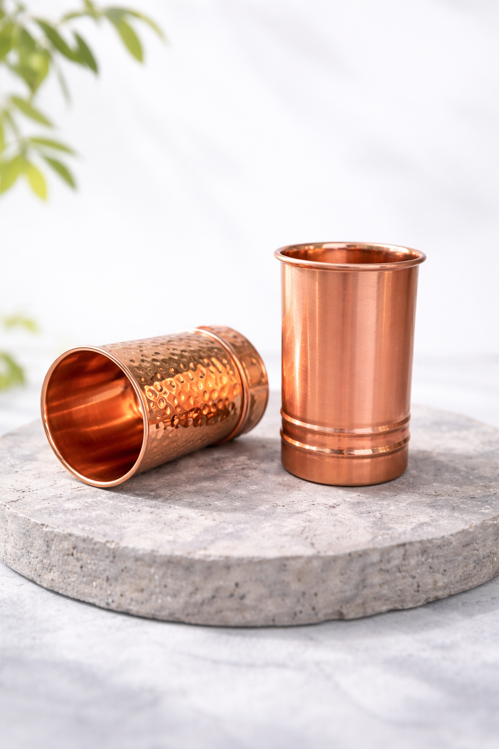 Tāmpatra copper glasses styled on a stone coaster, one glass resting on its side