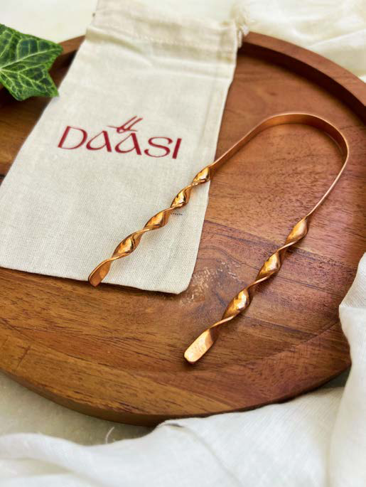 Jibbhi copper tongue cleaner on a wooden tray with its DAASI cotton pouch